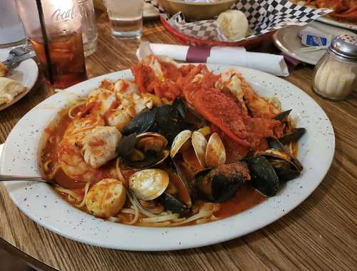 A large plate of seafood pasta with shrimp, mussels, clams, and a rich tomato sauce, served with bread rolls.