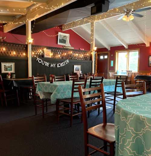 Cozy restaurant interior with blue tablecloths, wooden chairs, and string lights, featuring a playful sign: "You're my lobster."