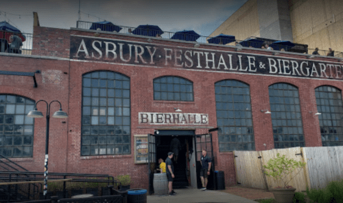 A brick building with large windows, featuring a sign for "Bierhalle" and outdoor seating with umbrellas on the rooftop.