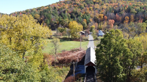 A scenic view of a covered bridge surrounded by vibrant autumn foliage and a rural landscape.