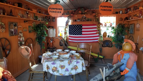 Cozy room decorated with pumpkins, an American flag, and a table set for a meal, featuring a scarecrow figure.