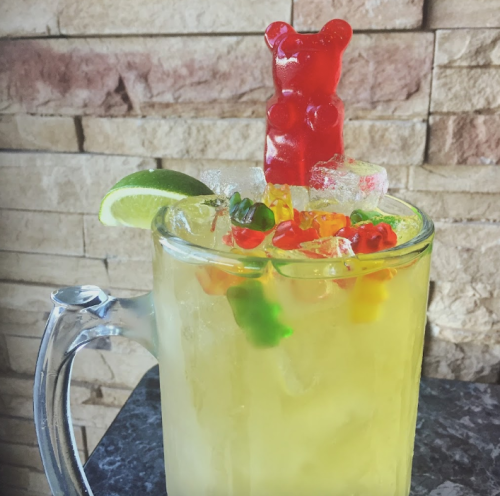 A colorful drink with ice, garnished with a lime slice and topped with a gummy bear and assorted gummy candies.