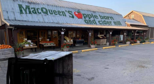 Exterior of MacQueen's Apple Barn and Cider Mill, featuring a rustic building with produce displays and autumn decorations.