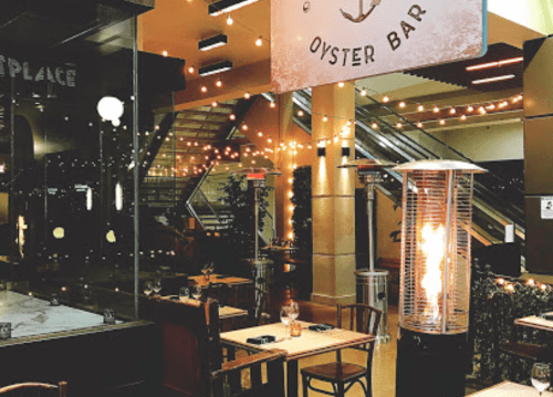Cozy oyster bar with warm lighting, outdoor seating, and a decorative heater in a modern setting.