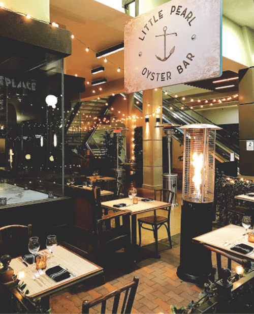 Cozy outdoor dining area at Little Pearl Oyster Bar, featuring tables, warm lighting, and a patio heater.