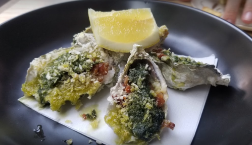A plate of baked oysters topped with herbs and a lemon wedge.