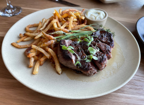 A plate of grilled steak with herbs, served alongside crispy fries and a small dish of sauce.