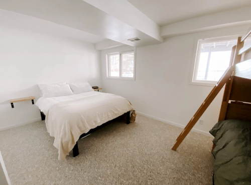 A bright, minimalist bedroom featuring a double bed, a bunk bed, and two windows.