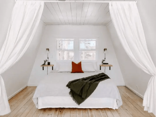 Cozy bedroom with a large bed, white curtains, wooden floors, and a decorative throw blanket.