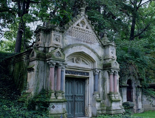 A weathered mausoleum with ornate architecture, surrounded by lush greenery and trees.