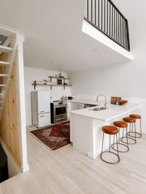 Modern kitchen with white cabinetry, stainless steel appliances, and a cozy rug, featuring a bar with three stools.