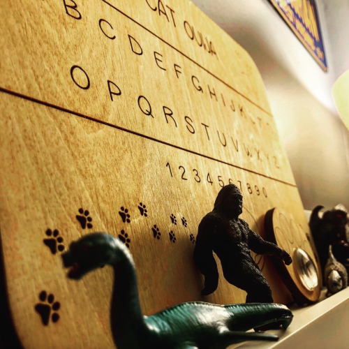 A wooden board with letters and numbers, featuring animal figurines and paw prints, set against a wall.