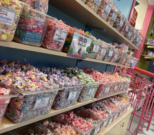 A colorful display of various candies in clear containers on wooden shelves in a candy shop.