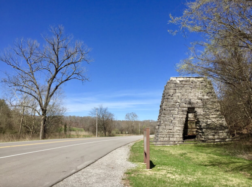 A stone structure beside a road, with bare trees and a clear blue sky in the background.