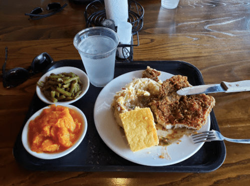 A tray with fried chicken, cornbread, mashed potatoes, green beans, and sweet potato mash, alongside a glass of water.