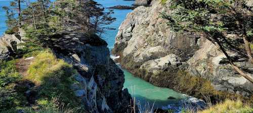 A serene coastal scene featuring rocky cliffs, lush greenery, and turquoise water flowing between the rocks.