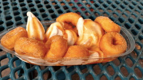 A plastic tray filled with mini donuts topped with soft serve ice cream and drizzled with caramel sauce.