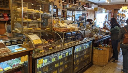A cozy shop interior with glass displays of candies and snacks, and customers browsing the selection.