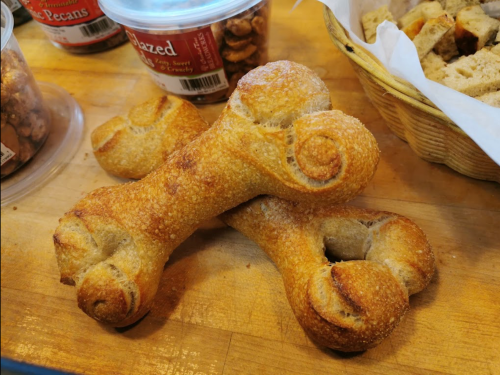 Two bone-shaped pastries dusted with sugar, resting on a wooden surface, surrounded by jars of nuts.