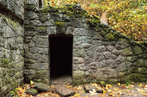 A moss-covered stone wall with an arched doorway, surrounded by autumn leaves and trees.
