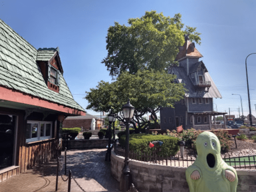 A whimsical scene featuring a green ghost figure, a quirky house, and lush greenery under a clear blue sky.