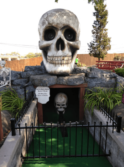 A large skull entrance to a mini-golf course, surrounded by rocks and greenery, with a smaller skull inside.