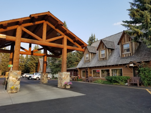 A rustic lodge with a wooden entrance and stone accents, surrounded by trees and parked cars.