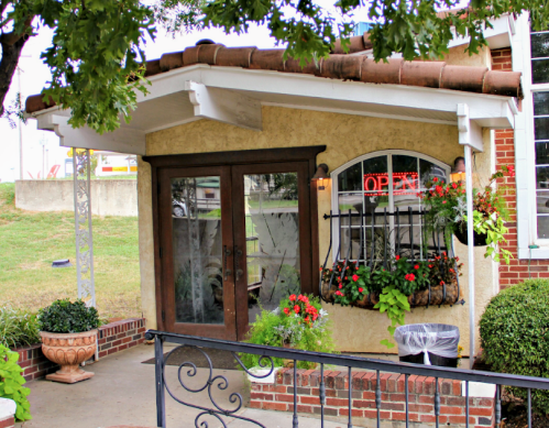 A charming building entrance with a "OPEN" sign, surrounded by greenery and flower pots.