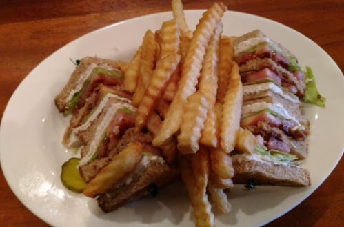 A plate of club sandwiches with layers of meat and lettuce, accompanied by a side of crinkle-cut fries.