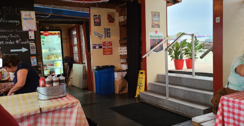 Interior of a casual eatery with checkered tablecloths, a counter, and potted plants near the entrance.