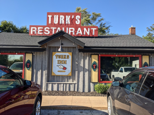 Exterior of Turk's Restaurant with a wooden facade and a sign featuring "Turk's Inn," surrounded by parked cars.