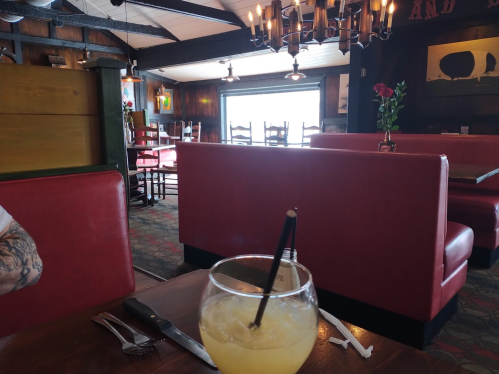 A cozy restaurant interior with red booths, a view of the outside, and a drink on the table.