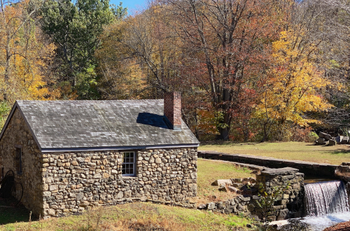 A stone cottage beside a small waterfall, surrounded by colorful autumn trees.