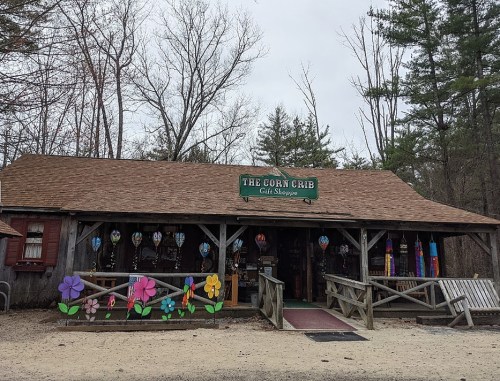 A rustic gift shop called "The Corn Crib" with colorful flower decorations and a wooden exterior, surrounded by trees.