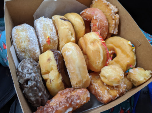A box filled with various donuts, including glazed, chocolate-covered, and sprinkled varieties.