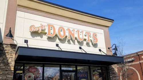 Sign for Ray's Donuts on a storefront, featuring a blue sky and a modern building design.