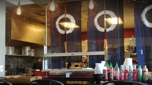Interior of a restaurant kitchen with blue curtains, hanging lights, and a counter displaying various sauces.