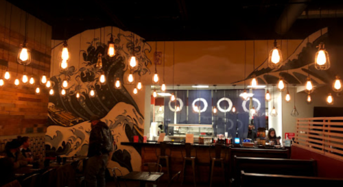 A cozy restaurant interior featuring a wave mural, warm lighting, and a bar area with patrons.