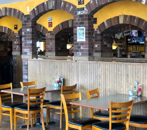 Interior of a restaurant featuring wooden tables and chairs, brick arches, and yellow walls.