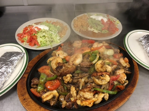 Sizzling fajitas with shrimp and meat, served with plates of rice, guacamole, and fresh salad.