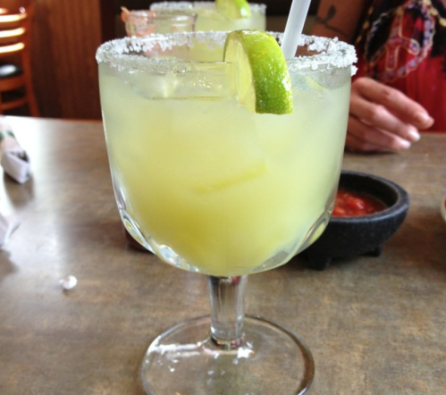 A close-up of a margarita in a glass with a salted rim and a lime wedge, set on a table.