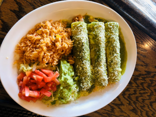 A plate of three green enchiladas topped with cheese, served with rice, guacamole, lettuce, and diced tomatoes.