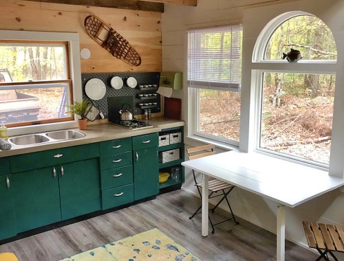 Cozy kitchen with green cabinets, a white table, and large windows overlooking a wooded area.