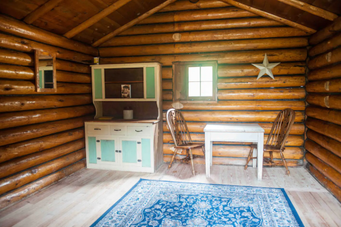 Cozy log cabin interior featuring a wooden table, two chairs, a sideboard, and a decorative rug.