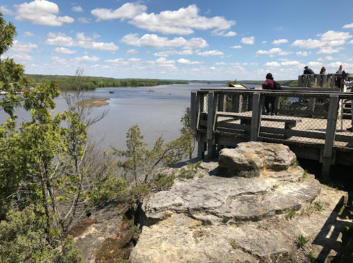 A scenic view from a wooden overlook, featuring a river and lush greenery under a partly cloudy sky.