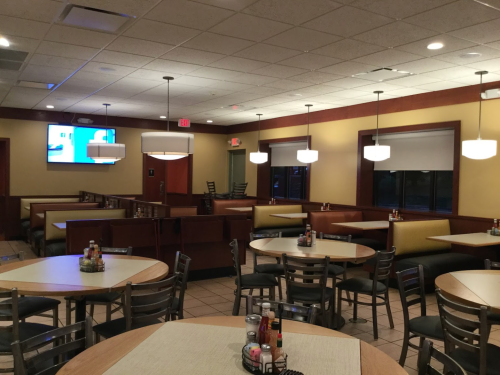 Interior of a restaurant featuring empty tables, booths, and a TV on the wall, with warm lighting and a cozy atmosphere.