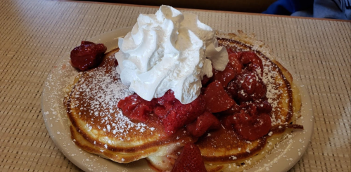 A plate of pancakes topped with whipped cream and strawberry sauce, garnished with fresh strawberries.
