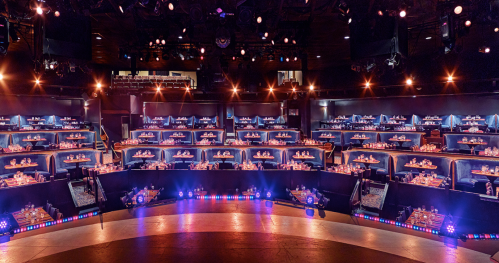 A theater stage with multiple rows of tables set for dining, illuminated by colorful stage lights.
