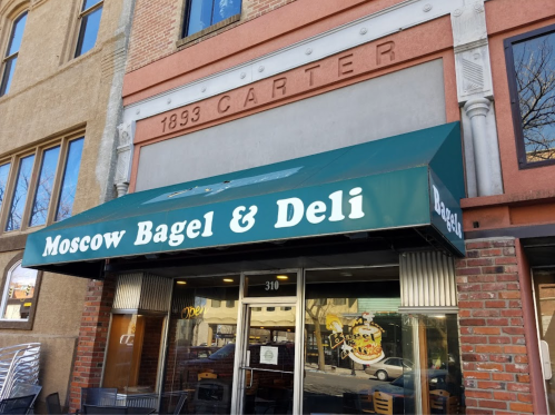 Green awning with "Moscow Bagel & Deli" sign above a brick storefront in a city setting.
