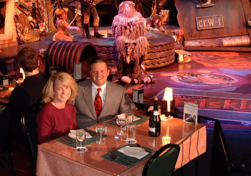 A couple sits at a table in a lively restaurant with a stage performance in the background.